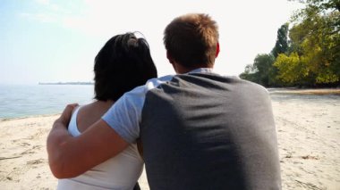 Kumsalda tahta kütüğün üzerinde otururken mutlu çift kucaklaşması. Güneşli bir günde deniz manzarasına hayran olan romantik bir çift. Sevgililer tatil köyünde birlikte vakit geçirirler. Yaz tatili ya da tatil kavramı. Yavaş çekim