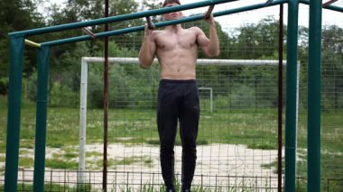 Genç kaslı sporcu spor alanında barfiks çekiyor. Atletik adam dışarıda egzersiz yapıyor. Yaz doğasında spor yapan güçlü bir adam. Sağlıklı ve aktif yaşam tarzı kavramı. Yavaş çekim