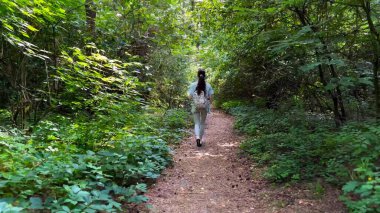 Genç bir kadın yaz ormanında patika boyunca gidiyor. Sırt çantalı bir kadın vahşi doğada patikaların arasında yürüyor. Tanınmayan bir kız dışarıda gezmekten zevk alıyor. Manzaraya hayran kalıyor. Kapat.