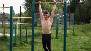 Spor sahasında barfiks çeken kaslı bir sporcu. Genç üstsüz sporcu doğada egzersiz yapıyor. Güçlü sporcu adam dışarıda antrenman yapıyor. Sağlıklı ve aktif yaşam tarzı kavramı. Yavaş çekim