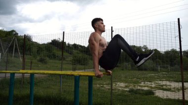 Spor alanında paralel barlarda karın kaslarını çalıştıran güçlü bir adam. Genç üstsüz sporcu doğada egzersiz yapıyor. Doğada spor yapan sporcu. Aktif spor yaşam tarzı kavramı.