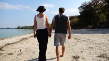 Romantik çift el ele tutuşup kıyı şeridinde yürüyor. Güneşli bir günde deniz kıyısına giden mutlu bir çift. Sevgililer tatil köyünde birlikte vakit geçirirler. Tatil ya da tatil kavramı. Yavaş çekim