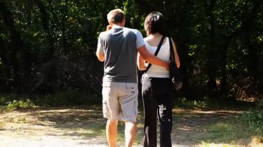 Mutlu çift yaz ormanında yolda yürüyor. Vahşi ormanlık alanda romantik bir çift geziyor. Sevgililer doğada birlikte vakit geçirirler. Aşk ve mutluluk kavramı. Yavaş çekim