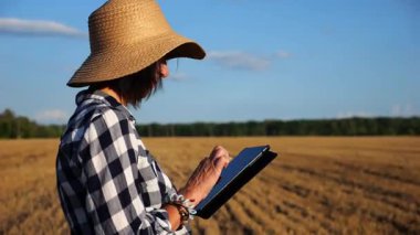 Yetişkin çiftçi güneşli bir günde buğday çayırında dijital tablet kullanıyor. Kadın tarım uzmanı arpa tarlasında hasat gözlemliyor. Güzel manzara manzarası. Tarım sektörü kavramı. Yavaş çekim