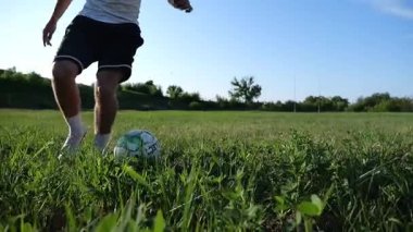 Profesyonel futbolcunun erkek ayağı, yeşil sahada koşarken topla numaralar gösterir. Güneşli bir günde Meadow 'da koşan sporcu bacakları topa vurur. Stadyumda antrenman yapan genç adam. Yavaş çekim