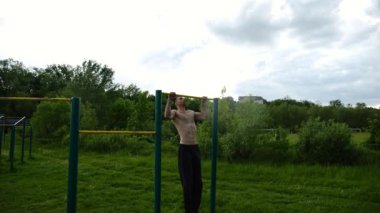 Spor sahasında barfiks çeken kaslı bir sporcu. Genç üstsüz sporcu doğada egzersiz yapıyor. Güçlü sporcu adam dışarıda antrenman yapıyor. Sağlıklı ve aktif yaşam tarzı kavramı. Yavaş çekim