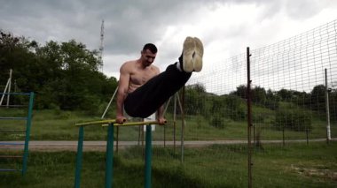 Güçlü bir adam karın kaslarını eğitir spor sahasında paralel barlarda bacak kaldırır. Genç üstsüz sporcu doğada egzersiz yapıyor. Doğada spor yapan sporcu. Sportif yaşam tarzı kavramı.