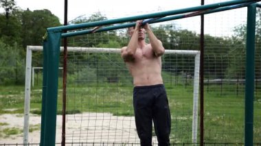 Genç kaslı sporcu spor alanında barfiks çekiyor. Atletik adam dışarıda egzersiz yapıyor. Yaz doğasında spor yapan güçlü bir adam. Sağlıklı ve aktif yaşam tarzı kavramı. Yavaş çekim