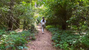 Genç bir kadın yaz ormanında patika boyunca gidiyor. Sırt çantalı bir kadın vahşi doğada patikaların arasında yürüyor. Tanınmayan bir kız dışarıda gezmekten zevk alıyor. Manzaraya hayran kalıyor. Kapat.