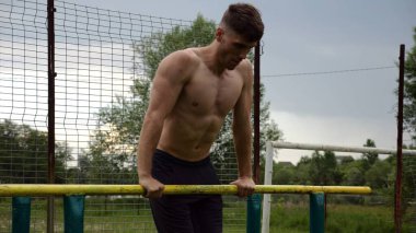 Erkek üstsüz sporcu doğada paralel barlarda şınav çekiyor. Spor alanında egzersiz yapan güçlü bir sporcu. Genç sporcu dışarıda sıkı çalışıyor. Aktif spor yaşam tarzı kavramı. Yavaş çekim