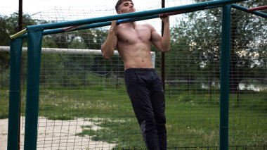 Genç kaslı sporcu spor alanında barfiks çekiyor. Atletik adam dışarıda egzersiz yapıyor. Yaz doğasında spor yapan güçlü bir adam. Sağlıklı ve aktif yaşam tarzı kavramı. Yavaş çekim