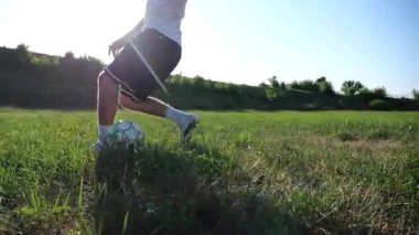Profesyonel futbolcunun erkek ayağı, yeşil sahada koşarken topla numaralar gösterir. Güneşli bir günde Meadow 'da koşan sporcu bacakları topa vurur. Stadyumda antrenman yapan genç adam. Yavaş çekim