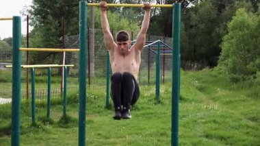 Spor sahasında karın kaslarını çalıştıran güçlü bir adam. Genç sporcu, barfiks çekme çubuğunda egzersiz yapıyor. Doğada spor yapan sporcu. Sportif yaşam tarzı kavramı.