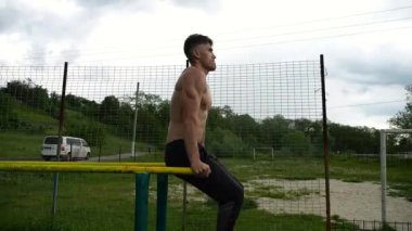 Spor alanında paralel barlarda karın kaslarını çalıştıran güçlü bir adam. Genç üstsüz sporcu doğada egzersiz yapıyor. Doğada spor yapan sporcu. Aktif spor yaşam tarzı kavramı.