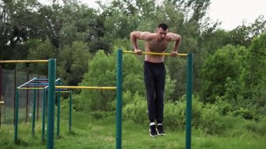 Güçlü ve kaslı bir adam doğanın yatay çubuğunda egzersiz yapıyor. Spor sahasında sıkı gömleksiz sporcu. Genç atletik adam dışarıda egzersiz yapıyor. Sağlıklı yaşam tarzı kavramı.