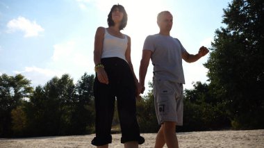 Romantik çift el ele tutuşup kıyı şeridinde yürüyor. Güneşli bir günde deniz kıyısına giden mutlu bir çift. Sevgililer tatil köyünde birlikte vakit geçirirler. Tatil ya da tatil kavramı. Yavaş çekim