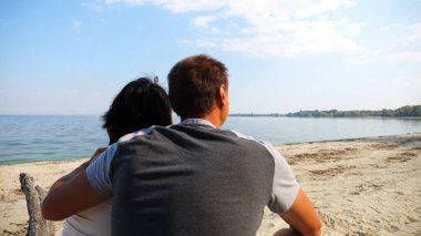 Kumsalda tahta kütüğün üzerinde otururken mutlu çift kucaklaşması. Güneşli bir günde deniz manzarasına hayran olan romantik bir çift. Sevgililer tatil köyünde birlikte vakit geçirirler. Yaz tatili ya da tatil kavramı. Yavaş çekim