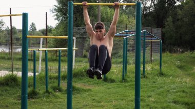 Spor sahasında karın kaslarını çalıştıran güçlü bir adam. Genç sporcu, barfiks çekme çubuğunda egzersiz yapıyor. Doğada spor yapan sporcu. Sportif yaşam tarzı kavramı.