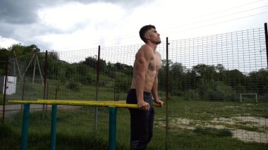 Genç sporcu doğada paralel barlarda şınav çekiyor. Spor alanında egzersiz yapan güçlü bir sporcu. Erkek üstsüz sporcu dışarıda sıkı çalışıyor. Aktif spor yaşam tarzı kavramı. Yavaş çekim