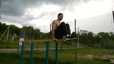 Spor alanında paralel barlarda karın kaslarını çalıştıran güçlü bir adam. Genç üstsüz sporcu doğada egzersiz yapıyor. Doğada spor yapan sporcu. Aktif spor yaşam tarzı kavramı.