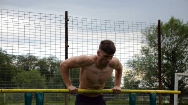 Erkek üstsüz sporcu doğada paralel barlarda şınav çekiyor. Spor alanında egzersiz yapan güçlü bir sporcu. Genç sporcu dışarıda sıkı çalışıyor. Aktif spor yaşam tarzı kavramı. Yavaş çekim