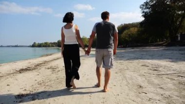 Romantik çift el ele tutuşup kıyı şeridinde yürüyor. Güneşli bir günde deniz kıyısına giden mutlu bir çift. Sevgililer tatil köyünde birlikte vakit geçirirler. Tatil ya da tatil kavramı. Yavaş çekim