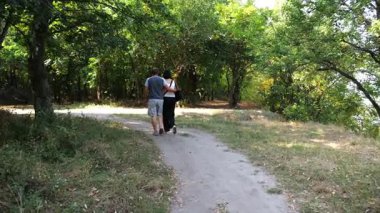 Mutlu çift yaz ormanında yolda yürüyor. Vahşi ormanlık alanda romantik bir çift geziyor. Sevgililer doğada birlikte vakit geçirirler. Aşk ve mutluluk kavramı. Yavaş çekim