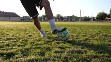 Profesyonel futbolcunun erkek ayağı, yeşil sahada koşarken topla numaralar gösterir. Sporcu bacakları gün batımında çayırda koşarken topa vurur. Stadyumda antrenman yapan genç adam. Yavaş çekim