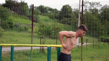 Genç sporcu doğada paralel barlarda şınav çekiyor. Spor alanında egzersiz yapan güçlü bir sporcu. Erkek üstsüz sporcu dışarıda sıkı çalışıyor. Aktif spor yaşam tarzı kavramı. Yavaş çekim