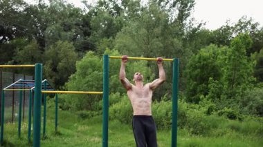 Güçlü ve kaslı bir adam doğanın yatay çubuğunda egzersiz yapıyor. Spor sahasında sıkı gömleksiz sporcu. Genç atletik adam dışarıda egzersiz yapıyor. Sağlıklı yaşam tarzı kavramı.