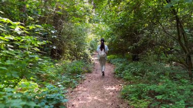 Genç bir kadın yaz ormanında patika boyunca gidiyor. Sırt çantalı bir kadın vahşi doğada patikaların arasında yürüyor. Tanınmayan bir kız dışarıda gezmekten zevk alıyor. Manzaraya hayran kalıyor. Kapat.