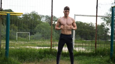 Spor sahasında çömelme hareketleri yapan erkek üstsüz atlet. Yaz doğasında çalışan genç bir sporcu. Güçlü sporcu dışarıda egzersiz yapıyor. Aktif ve sportif yaşam tarzı kavramı. Yavaş çekim