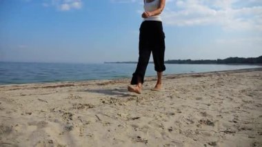 Güneşli bir günde sahilde kumsala giden mutlu yetişkin kadın. Arka planda sakin dalgalarla deniz kıyısında yürüyen güzel bir bayan. Yaz tatili ya da tatil kavramı. Yavaş çekim