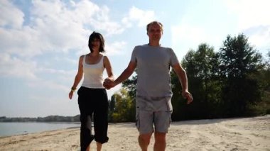 Romantik çift el ele tutuşuyor ve sahilde koşuyor. Güneşli bir günde deniz kıyısında koşan mutlu bir çift. Sevgililer tatil köyünde birlikte vakit geçirirler. Yaz tatili veya tatil kavramı.