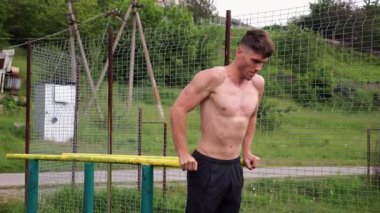 Genç sporcu doğada paralel barlarda şınav çekiyor. Spor alanında egzersiz yapan güçlü bir sporcu. Erkek üstsüz sporcu dışarıda sıkı çalışıyor. Aktif spor yaşam tarzı kavramı. Yavaş çekim
