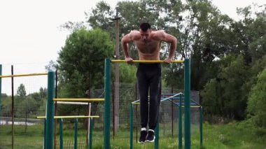 Cesur üstsüz sporcu doğada yatay çıtada şınav çekiyor. Güçlü ve kaslı adam spor alanında antrenman yapıyor. Genç atletik adam dışarıda egzersiz yapıyor. Aktif ve sağlıklı yaşam tarzı kavramı.