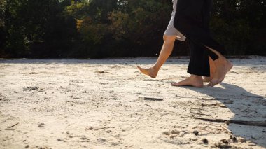 Çiftin erkek ve dişi bacakları kumlu sahilde yürüyor. Güneşli bir günde kumsalda yürüyen çıplak ayaklı bir çift. Sevgililer tatil köyünde birlikte vakit geçirirler. Yaz tatili veya tatil kavramı.