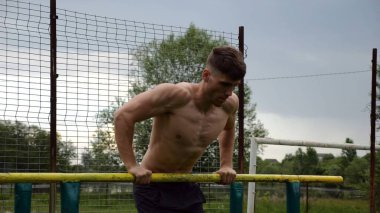 Erkek üstsüz sporcu doğada paralel barlarda şınav çekiyor. Spor alanında egzersiz yapan güçlü bir sporcu. Genç sporcu dışarıda sıkı çalışıyor. Aktif spor yaşam tarzı kavramı. Yavaş çekim