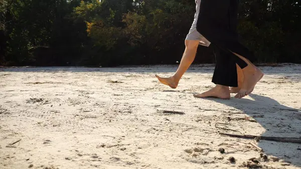 Çiftin erkek ve dişi bacakları kumlu sahilde yürüyor. Güneşli bir günde kumsalda yürüyen çıplak ayaklı bir çift. Sevgililer tatil köyünde birlikte vakit geçirirler. Yaz tatili veya tatil kavramı.