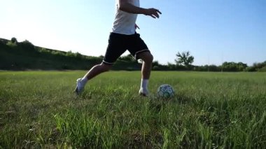 Üniformalı profesyonel futbolcu yeşil sahada koşarken topa numara yapıyor. Sporcu güneşli bir günde Meadow 'da koşarken topa vurur. Stadyumda antrenman yapan genç adam. Serbest stil futbol.