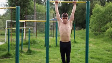 Spor sahasında karın kaslarını çalıştıran güçlü bir adam. Genç sporcu, barfiks çekme çubuğunda egzersiz yapıyor. Doğada spor yapan sporcu. Sportif yaşam tarzı kavramı.