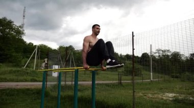 Spor alanında paralel barlarda karın kaslarını çalıştıran güçlü bir adam. Genç üstsüz sporcu doğada egzersiz yapıyor. Doğada spor yapan sporcu. Aktif spor yaşam tarzı kavramı.