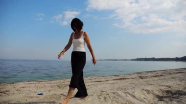 Güneşli bir günde sahilde kumsala giden mutlu yetişkin kadın. Arka planda sakin dalgalarla deniz kıyısında yürüyen güzel bir bayan. Yaz tatili ya da tatil kavramı. Yavaş çekim