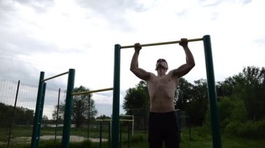 Spor sahasında barfiks çeken kaslı bir sporcu. Genç üstsüz sporcu doğada egzersiz yapıyor. Güçlü sporcu adam dışarıda antrenman yapıyor. Sağlıklı ve aktif yaşam tarzı kavramı. Yavaş çekim