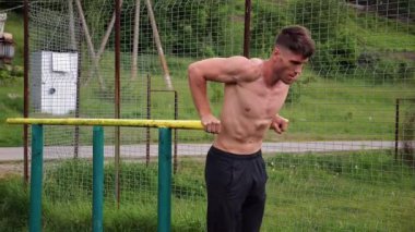 Genç sporcu doğada paralel barlarda şınav çekiyor. Spor alanında egzersiz yapan güçlü bir sporcu. Erkek üstsüz sporcu dışarıda sıkı çalışıyor. Aktif spor yaşam tarzı kavramı. Yavaş çekim