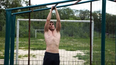 Genç kaslı sporcu spor alanında barfiks çekiyor. Atletik adam dışarıda egzersiz yapıyor. Yaz doğasında spor yapan güçlü bir adam. Sağlıklı ve aktif yaşam tarzı kavramı. Yavaş çekim