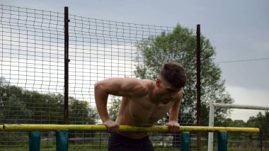 Erkek üstsüz sporcu doğada paralel barlarda şınav çekiyor. Spor alanında egzersiz yapan güçlü bir sporcu. Genç sporcu dışarıda sıkı çalışıyor. Aktif spor yaşam tarzı kavramı. Yavaş çekim