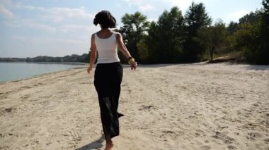 Güneşli bir günde sahilde koşan mutlu yetişkin kadın. Arka planda sakin dalgalarla deniz kıyısında koşan güzel bir bayan. Yaz tatili ya da tatil kavramı. Yavaş çekim