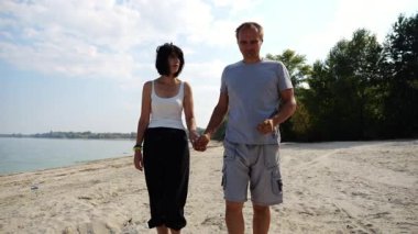 Güneşli bir günde deniz kıyısına giden mutlu bir çift. Romantik çift el ele tutuşup sahilde yürüyor. Sevgililer tatil köyünde birlikte vakit geçirirler. Yaz tatili ya da tatil kavramı. Yavaş çekim