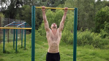 Spor sahasında barfiks çeken kaslı bir sporcu. Genç üstsüz sporcu doğada egzersiz yapıyor. Güçlü sporcu adam dışarıda antrenman yapıyor. Sağlıklı ve aktif yaşam tarzı kavramı. Yavaş çekim